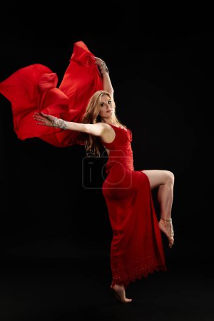 A beautiful woman in a red dress gracefully dances.