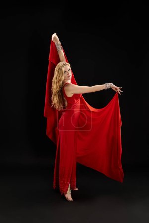 Photo for Young woman in red dress gracefully dancing, holding a red cloth. - Royalty Free Image