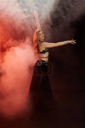 A mesmerizing young woman in a black dress gracefully dances amidst swirling smoke.