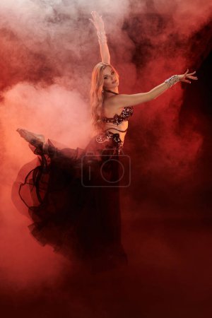 A graceful woman in a black dress dances amidst swirling smoke.