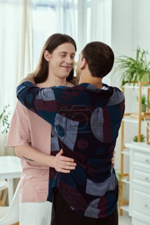 Photo for A gay couple in casual clothes hug each other warmly in a homely living room. - Royalty Free Image