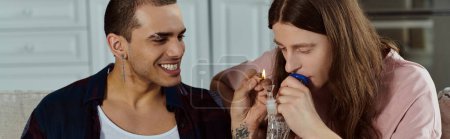 A gay couple, dressed casually, laughing joyfully together at home, lighting marijuana in the glass bong