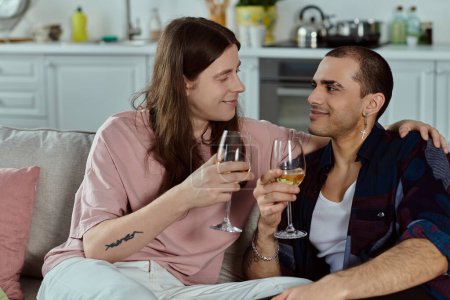 Photo for A gay couple dressed casually, sitting closely on a couch, sharing a quiet moment while holding wine glasses. - Royalty Free Image
