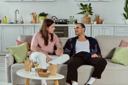 Téléchargez les photos : Un couple gay en vêtements décontractés ayant une conversation profonde tout en étant assis confortablement sur un canapé à la maison. - en image libre de droit