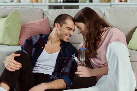 ein schwules Paar, sitzt glücklich auf einer gemütlichen Couch in lässiger Kleidung, genießt einen Moment der Zweisamkeit, lacht und hält eine Glasbong in der Hand