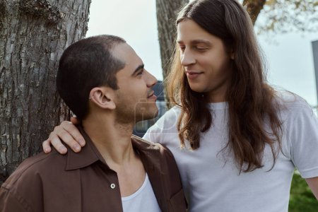 Téléchargez les photos : Un couple gay aimant, se tenir ensemble près d'un arbre en vêtements décontractés, profiter du temps de qualité en plein air. - en image libre de droit