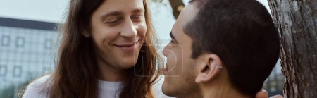 Téléchargez les photos : Casual couple gay debout paisiblement près d'un arbre, profiter du temps de qualité ensemble à l'extérieur. - en image libre de droit