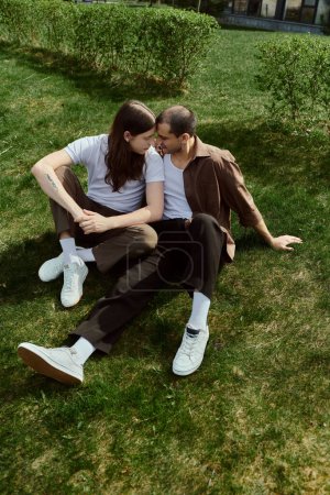 Photo for A gay couple, dressed casually, enjoying a serene moment together as they sit on the grass. - Royalty Free Image
