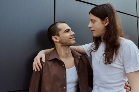 Téléchargez les photos : Un couple gay en vêtements décontractés se tenant étroitement ensemble, profitant d'un moment de connexion à l'extérieur. - en image libre de droit