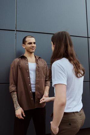 Foto de Pareja gay de pie juntos en frente de una pared texturizada, compartiendo un momento de conexión. - Imagen libre de derechos