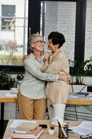 A mature lesbian couple, standing together, collaborating in an office setting.