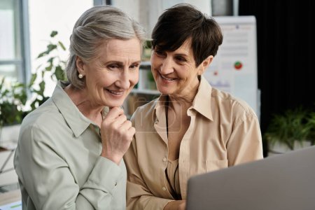 Two mature beautiful women engage in shared work on a laptop screen.