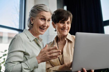 Two mature women closely examine a laptop screen in an office setting.