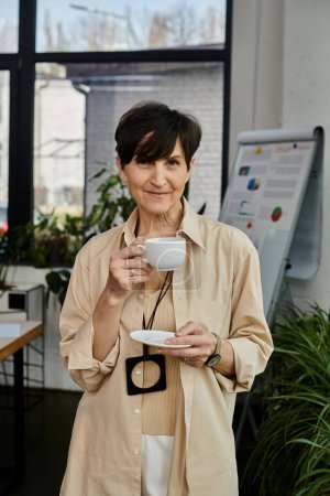 Une femme tient une tasse de café et regarde la caméra.