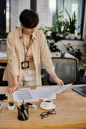 A woman stands at a desk surrounded by papers.