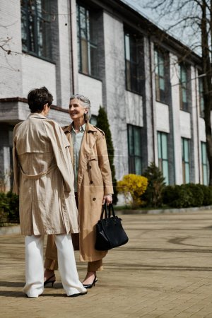 A mature, beautiful lesbian couple standing elegantly in front of a grand building.