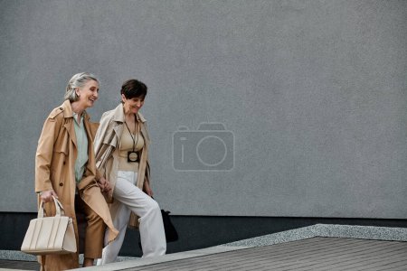 Zwei reife Frauen tragen Taschen und gehen den belebten Bürgersteig der Stadt entlang.
