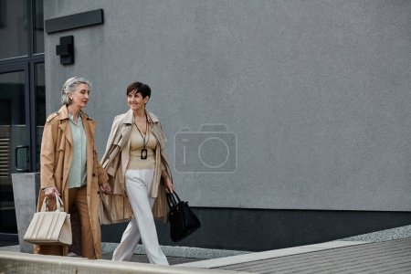 Zwei Frauen, ein reifes, schönes lesbisches Paar, gehen mit Taschen auf der Straße entlang.