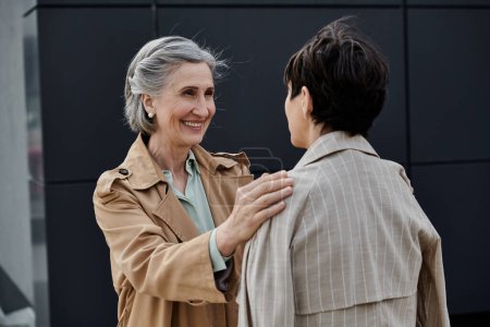 Mature, beautiful lesbian couple walking to office in trench coats.