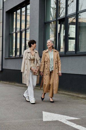 Foto de Two women, mature and beautiful, walk hand in hand down a bustling street. - Imagen libre de derechos