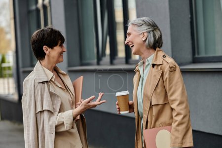 Two women engaging in conversation while holding coffee cups.