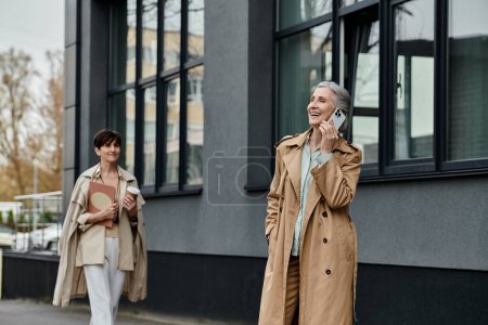Dos mujeres, madura hermosa pareja lesbiana, caminan por la calle hablando en sus teléfonos celulares.