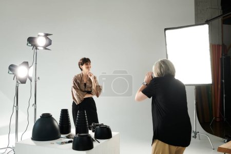 Middle-aged lesbian couple in a photo studio; one woman snapping a picture of her partner in front of the camera.