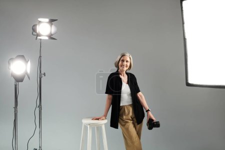 Middle aged photographer with digital camera striking a pose in photo studio