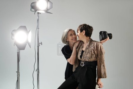 A middle-aged photographer snaps pictures as her partner poses in a photo studio.