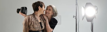 Middle-aged lesbian couple in a photo studio, a woman holds a camera next to a model.