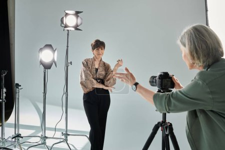 A middle-aged lesbian couple in a photo studio, one behind the camera and the other posing as the model.