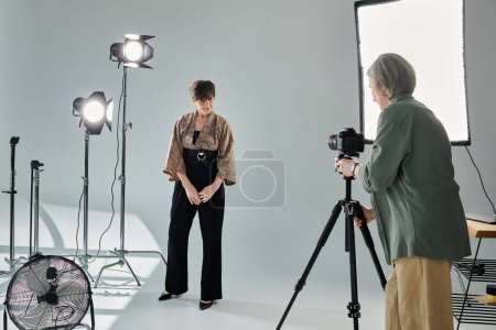 A middle-aged photographer captures her partner posing in a photo studio.