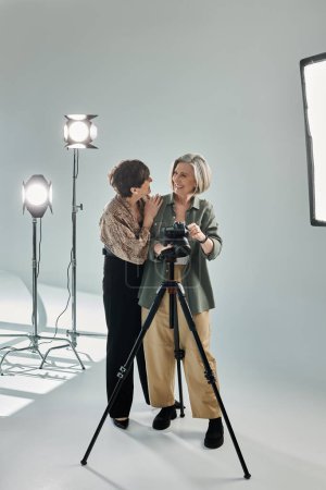 Ein lesbisches Paar mittleren Alters in einem Fotostudio; eine hinter der Kamera, die andere umarmt sie