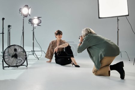 Eine Frau mittleren Alters kniet neben einem Ventilator in einem Fotostudio, während die Fotografin den Moment mit ihrer Kamera einfängt.