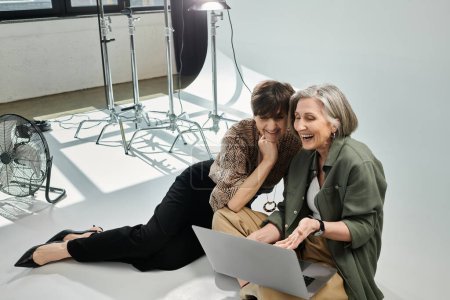Middle aged lesbian couple sitting peacefully on a white floor in a photo studio