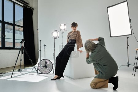 A middle aged lesbian couple in a studio, one setting up camera and the other getting ready as the model.