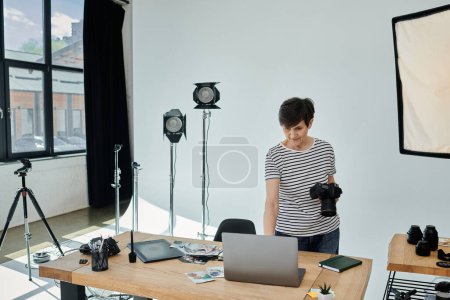 Middle-aged woman stands confidently, working on laptop in modern studio space.