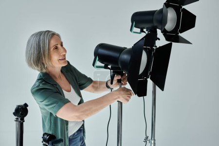 Middle-aged woman holds a light while setting up a tripod in a professional photo studio