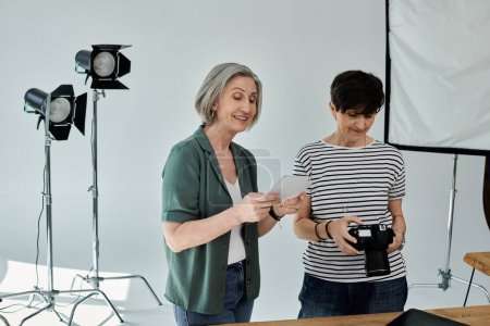 A middle-aged woman holds a camera in front of her partner in a professional modern photo studio.
