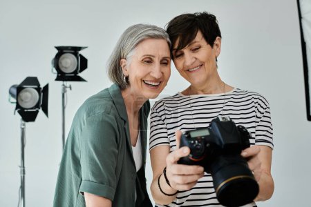Ein lesbisches Paar mittleren Alters macht fröhlich ein Foto mit einer Kamera in einem professionellen modernen Fotostudio.