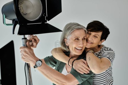 Middle-aged lesbian couple hug warmly in a professional photo studio in front of softbox