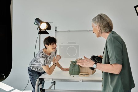 Une femme d'âge moyen se tient dans un studio photo moderne, souriant en travaillant ensemble devant un appareil photo.
