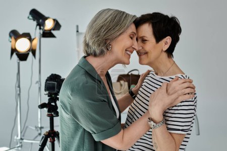 Zwei Frauen mittleren Alters umarmen sich in einem modernen Fotostudio und drücken vor der Kamera Liebe und Einheit aus.