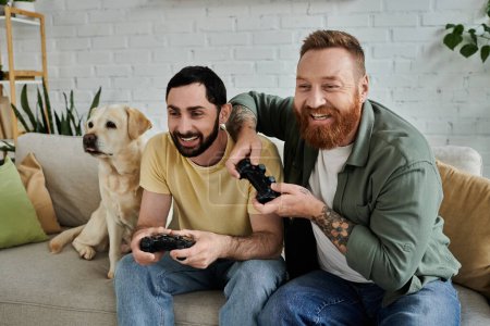 A bearded gay couple and their labrador dog sit on a couch intensively playing a video game together in the living room.