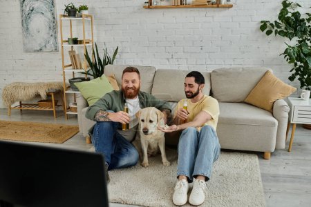 Two bearded men sit on a couch with their Labrador, enjoying a sport match together in their living room.