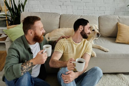 Two men, a bearded gay couple, holding coffee mugs near a Labrador dog in their living room.