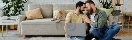Photo for Two men with beards sit on top of a couch working remotely, accompanied by a Labrador dog in a cozy living room. - Royalty Free Image