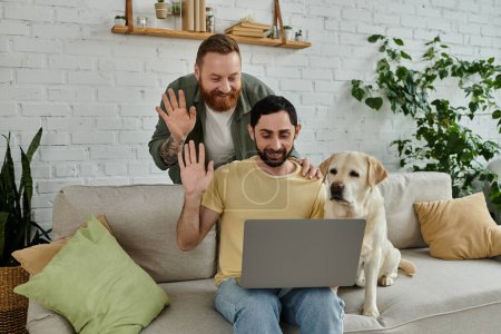 Bearded gay couple working remotely on laptop with labrador dog in cozy living room setting.