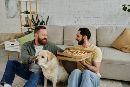 Zwei bärtige Männer sitzen auf dem Fußboden und essen Pizza, während ihr treuer Labrador-Hund in gemütlicher Wohnzimmeratmosphäre zu ihnen stößt..