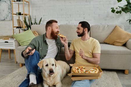 A gay couple and their labrador dog share a pizza on a cozy couch in the living room.
